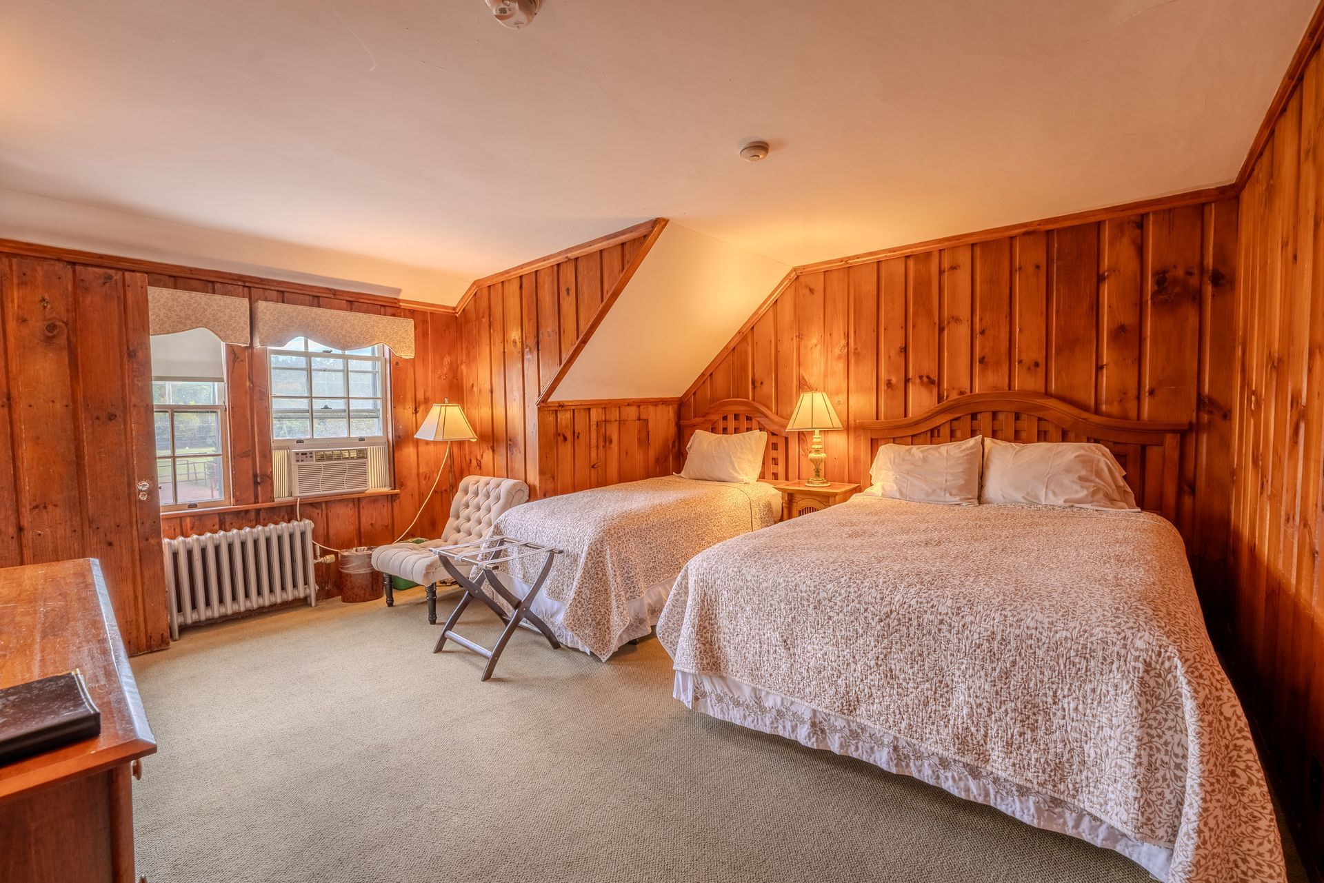 Bedroom with two beds, wood paneling, two windows, and a desk.
