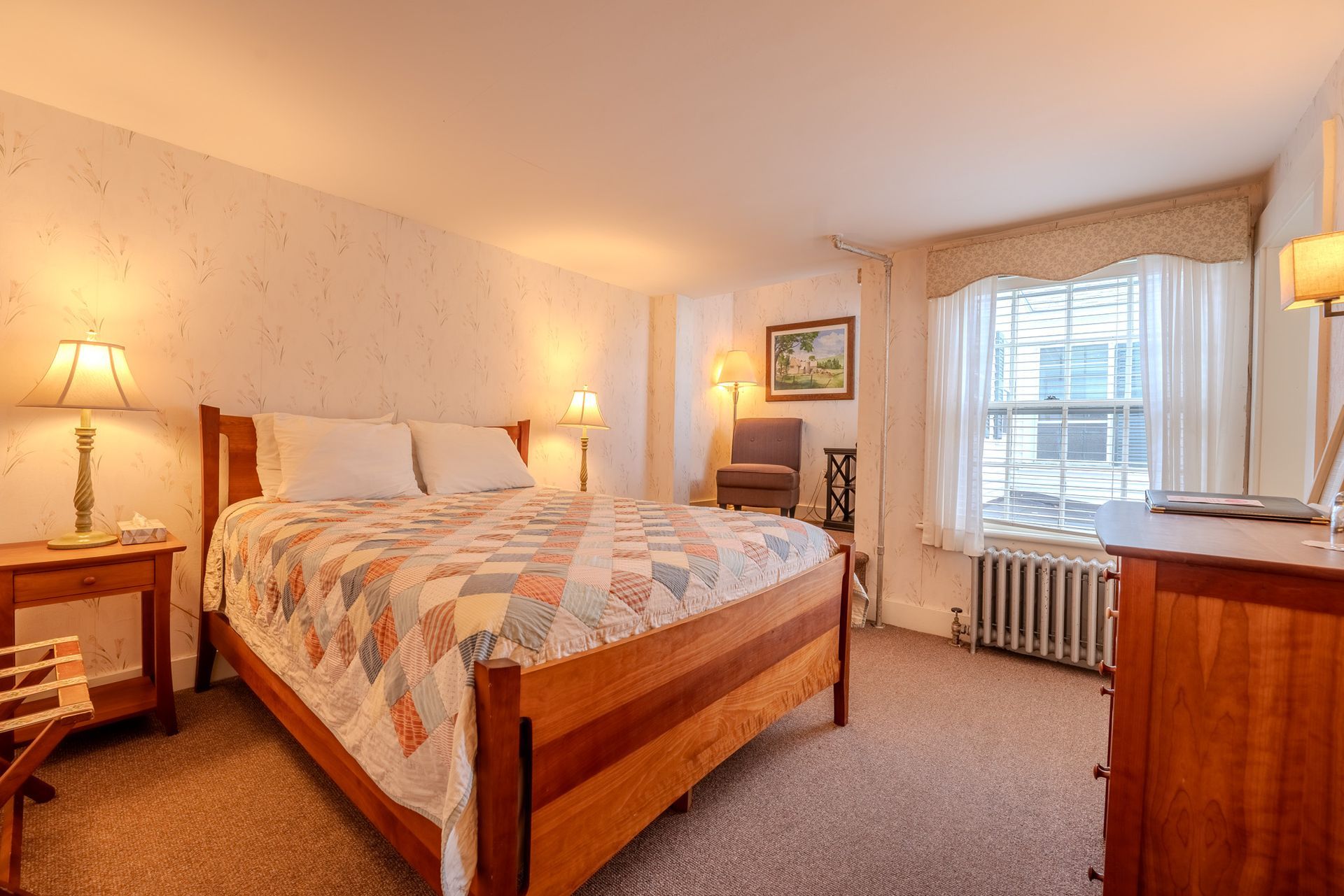 Bedroom with wooden bed, patchwork quilt, side tables, window, and dresser.