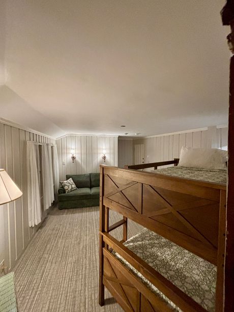 Cozy bedroom with bunk bed, green sofa, white curtains, and a sloped ceiling