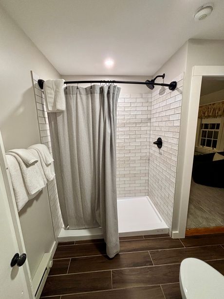 Small bathroom with walk-in shower, gray curtain, white tile, and dark wood-look floor.
