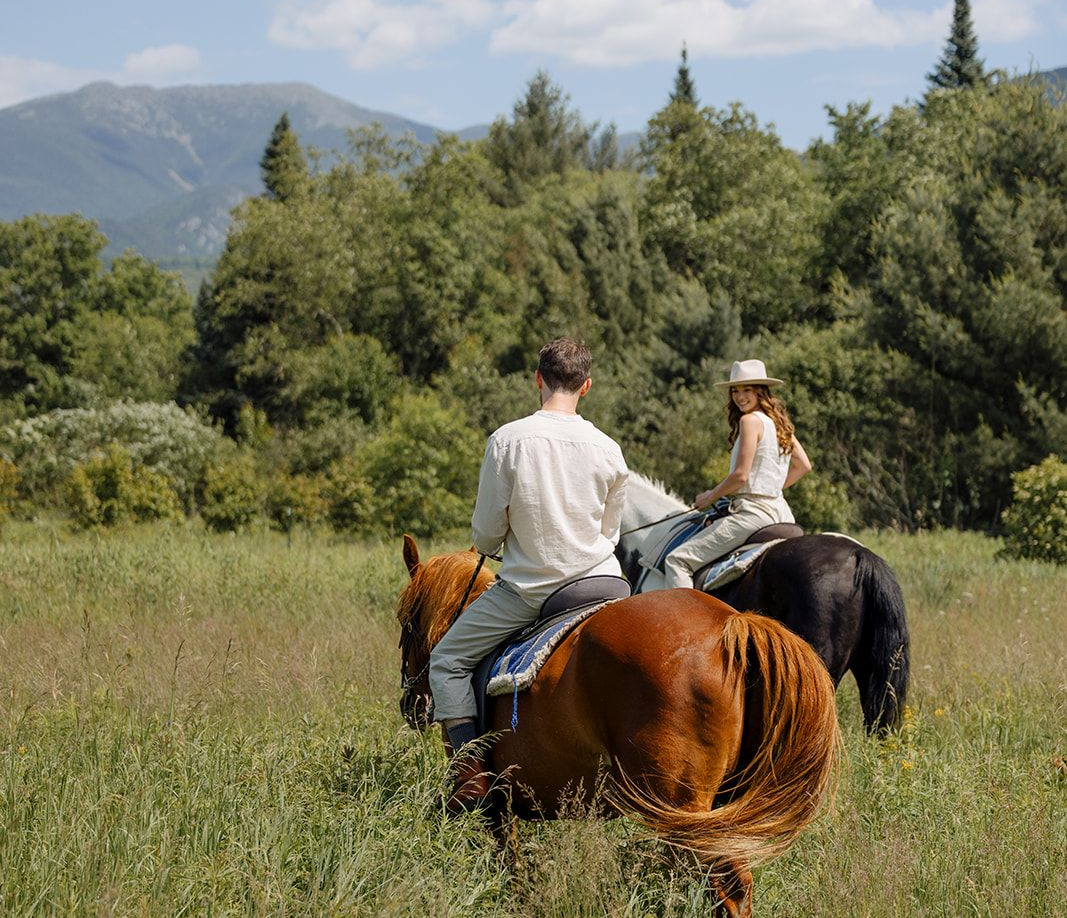 two riders on horseback in a field with mountains in the background
