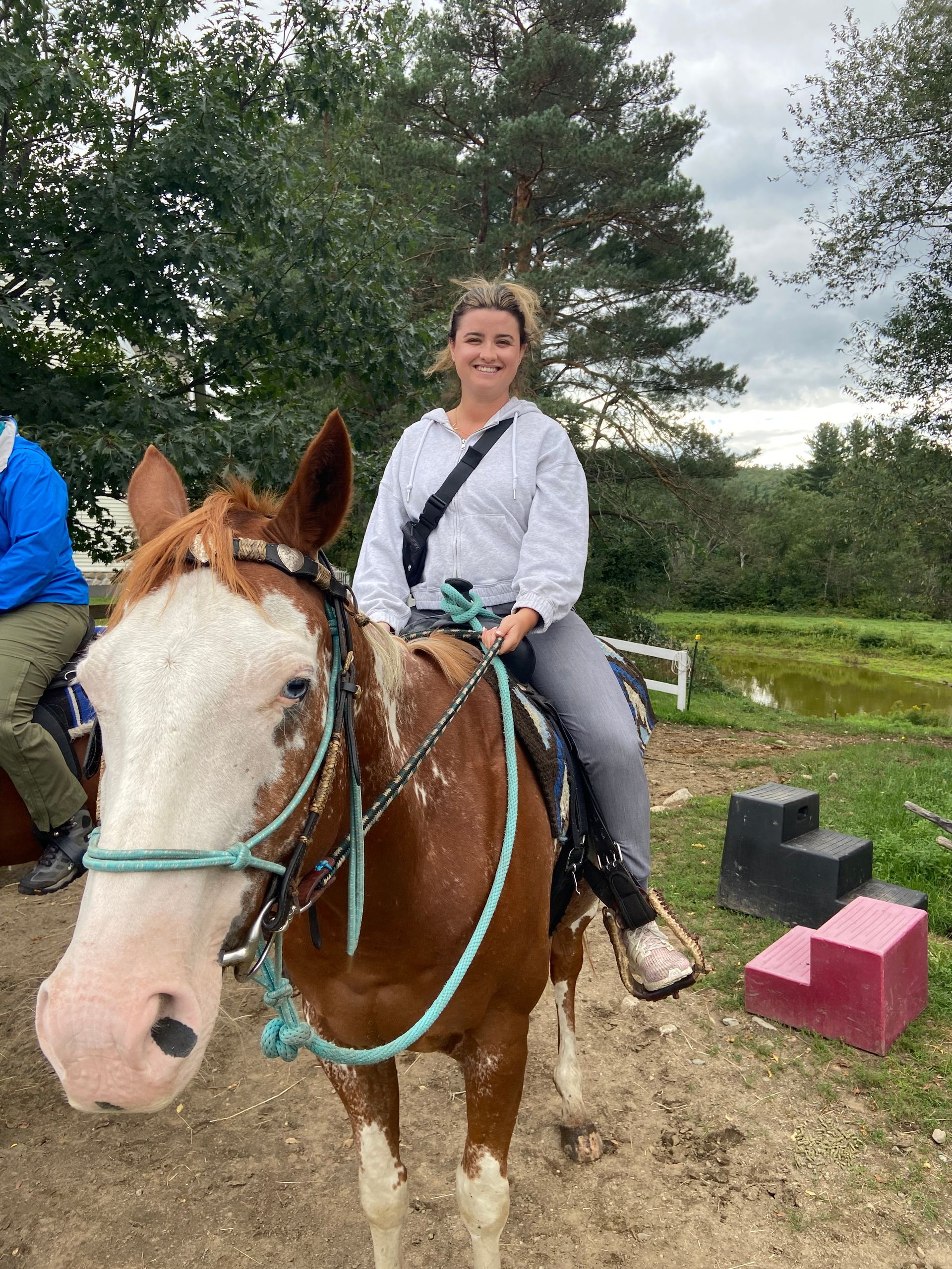 Smiling rider on a brown-and-white horse in a grassy outdoor area, with jumping blocks nearby