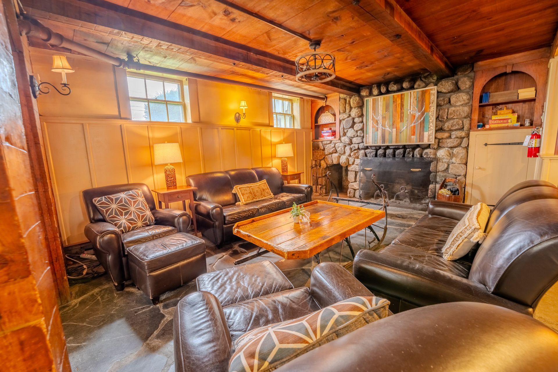 Cozy living room with stone fireplace, leather furniture, and wooden ceiling.