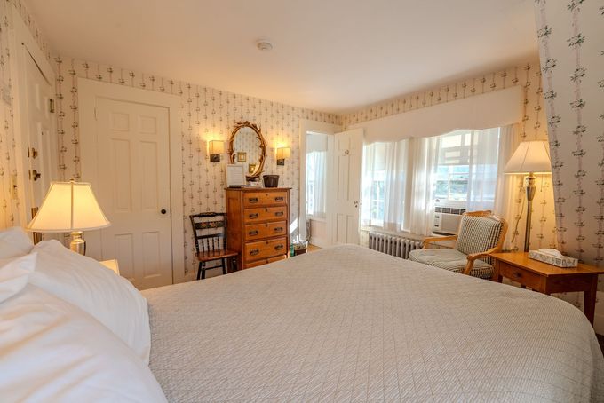 Cozy bedroom with white bedding, dresser, lamps, and floral wallpaper in warm light