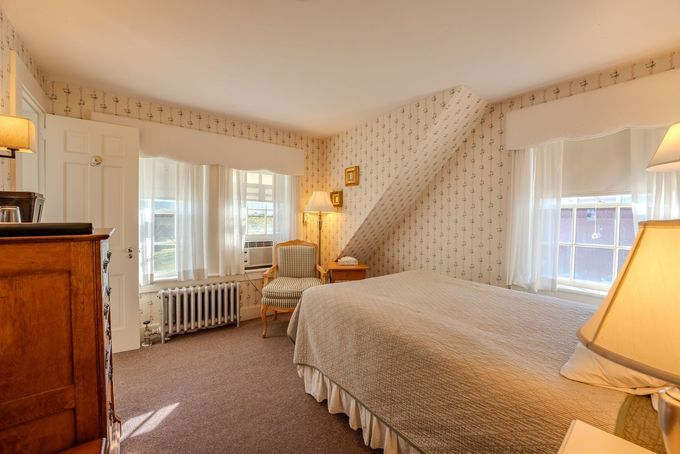 Cozy bedroom with two beds, dresser, lamps, and windows with sheer curtains