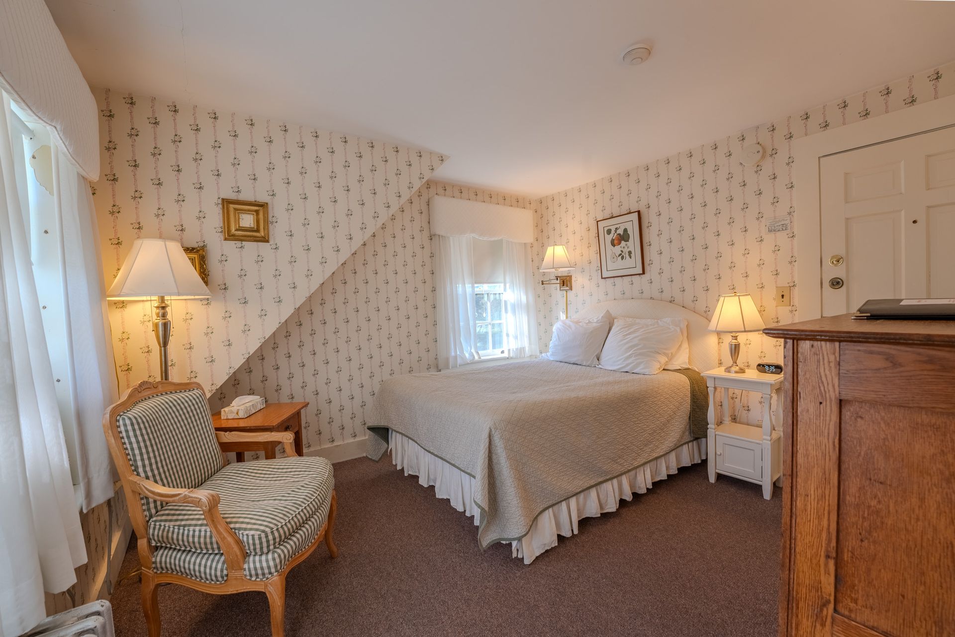 Bedroom with bed, chair, and dresser, with floral wallpaper and soft lighting.