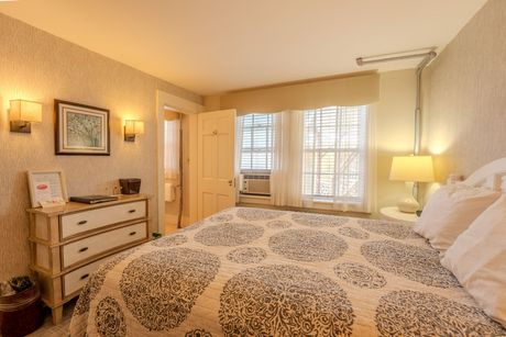 Cozy bedroom with a bed, dresser, and windows, lit by lamps.