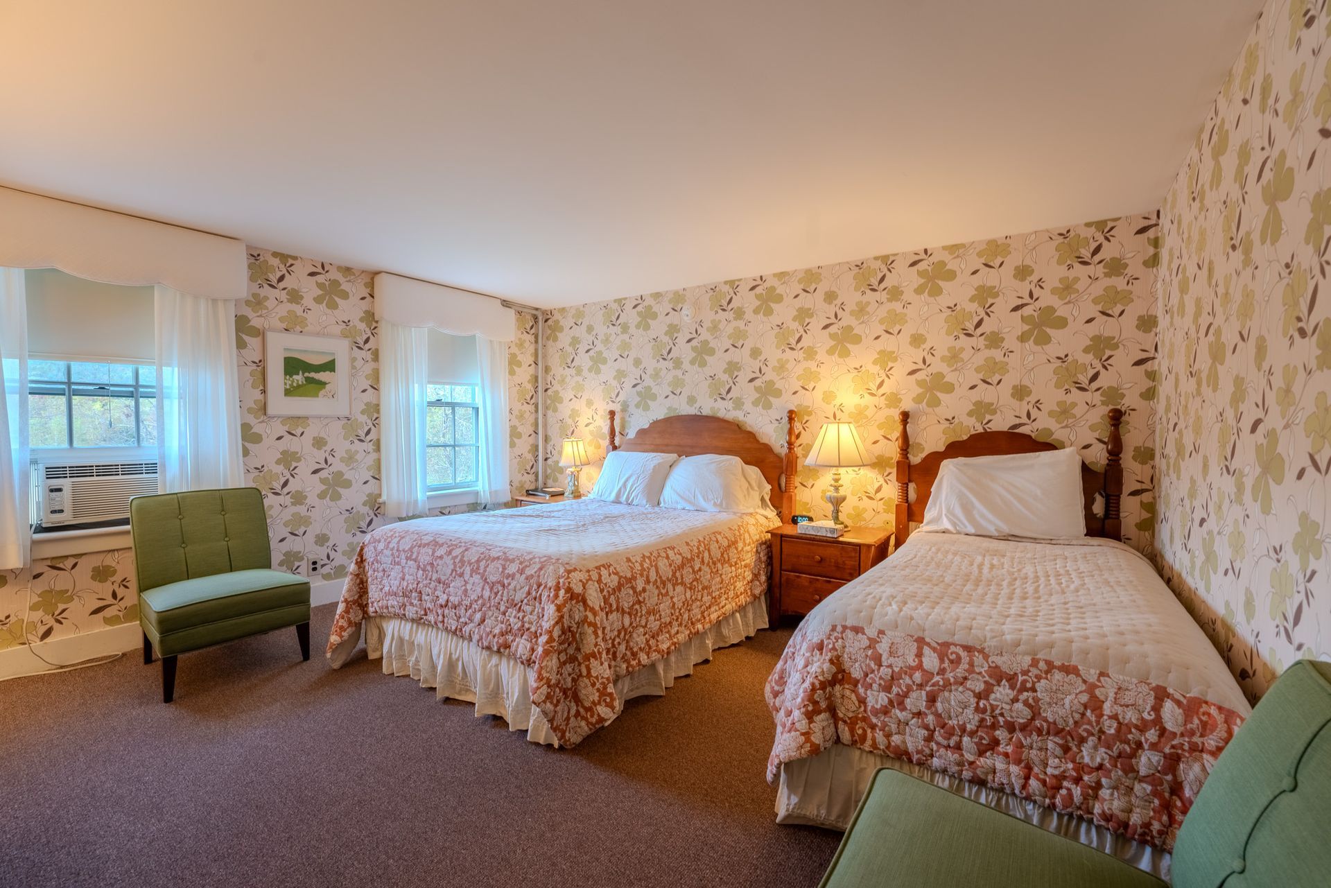Bedroom with two beds and a small green chair; floral wallpaper and pink bedspreads.