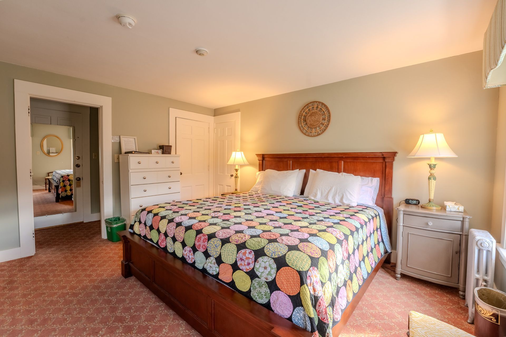 Bedroom with a queen-sized bed, colorful quilt, chest of drawers, and a doorway leading to another room.