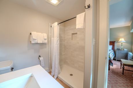 Bathroom with a white sink, shower, and towels. Bedroom visible in the doorway.