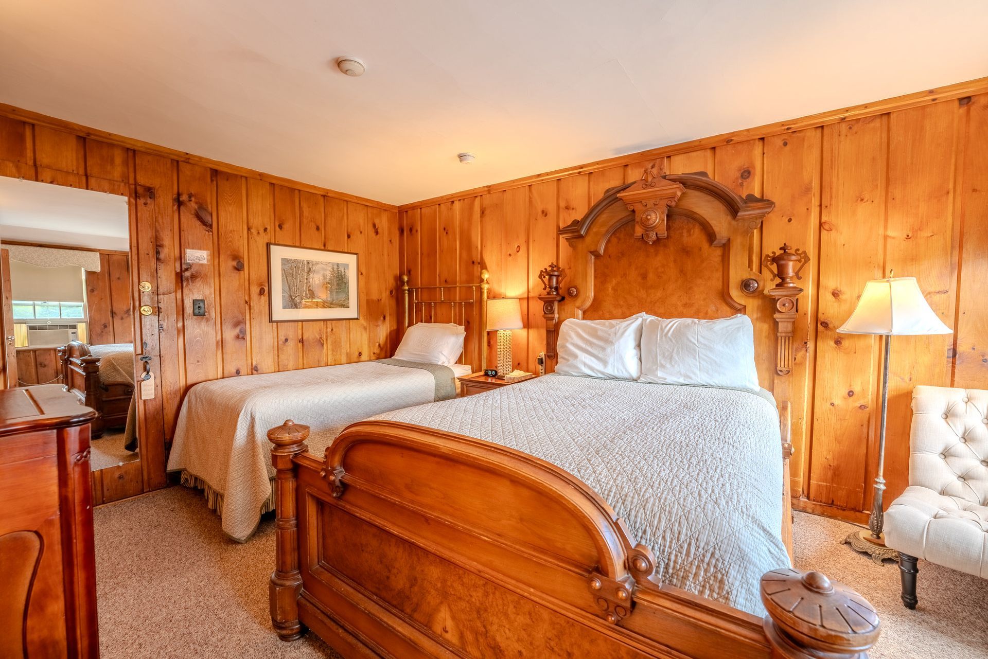 Wooden-paneled bedroom with a queen bed, twin bed, and armchair.