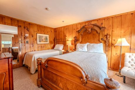 Bedroom with two wooden beds, wood-paneled walls, and a white armchair.