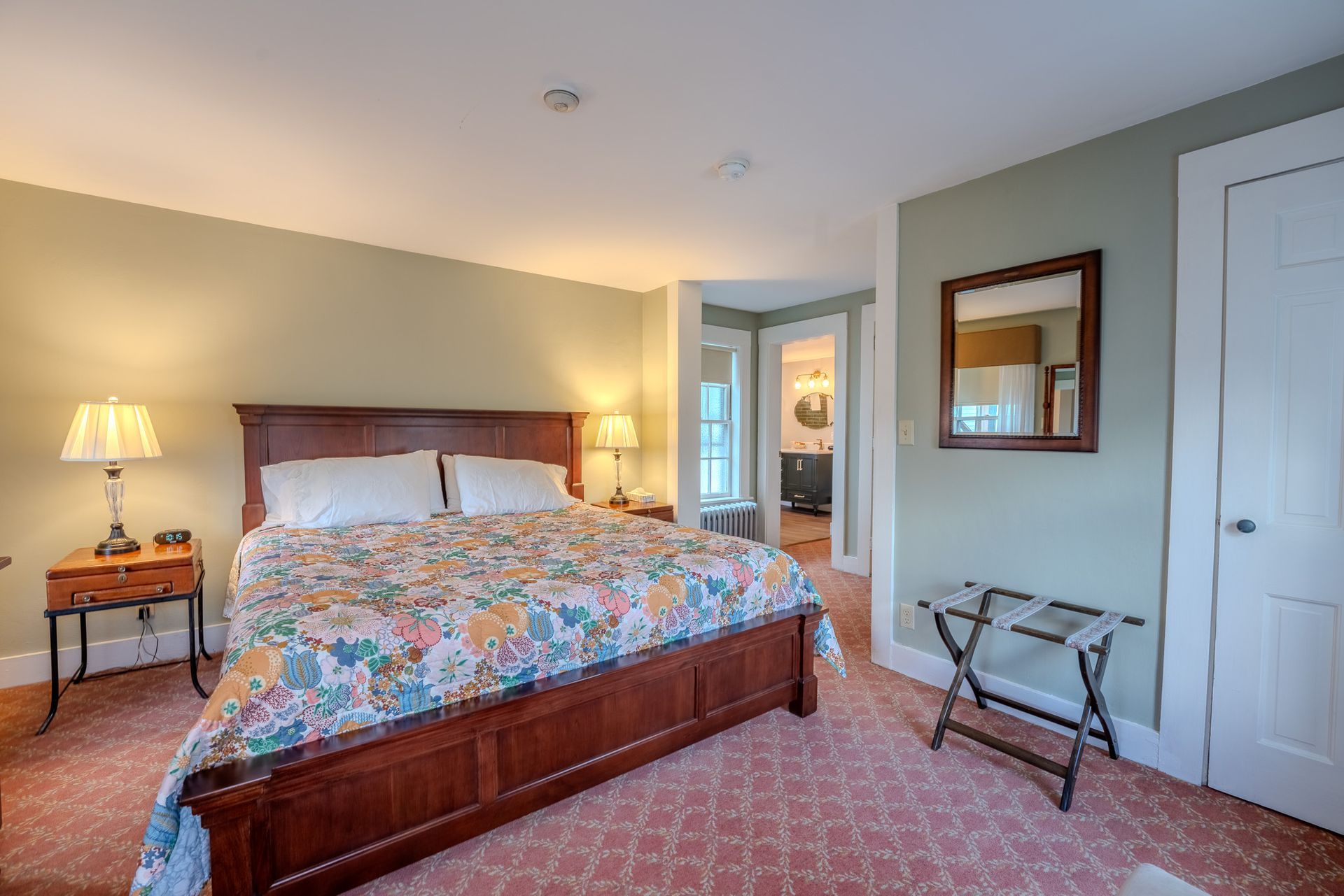 Bedroom with a wooden bed frame, floral bedding, and a view into an adjoining bathroom.