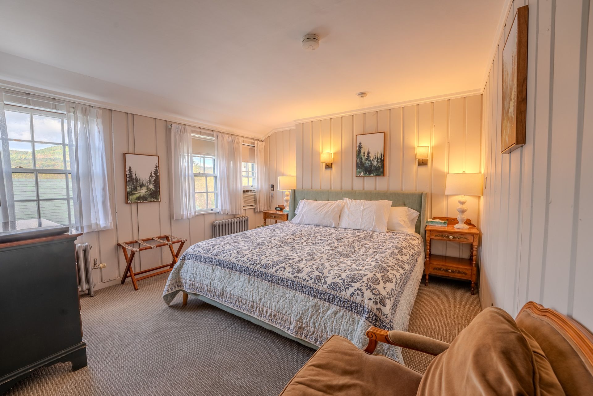 Cozy bedroom with a king-sized bed, side tables, artwork, and a chair by the window.