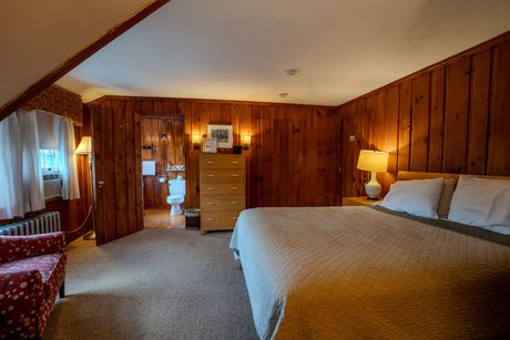 Bedroom with wood paneling, king bed, armchair, and bathroom access.