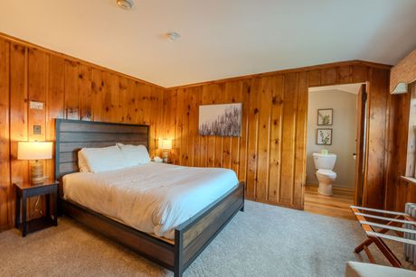 Bedroom with wood paneling, queen bed, and an open door to a bathroom.
