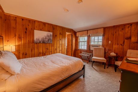 Bedroom with wood-paneled walls, a bed, two chairs, and a small table near a window.