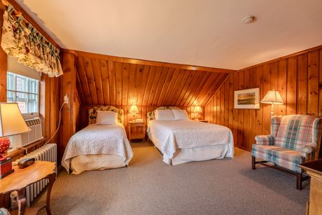 A bedroom with two beds, wood paneling, and a patterned armchair.