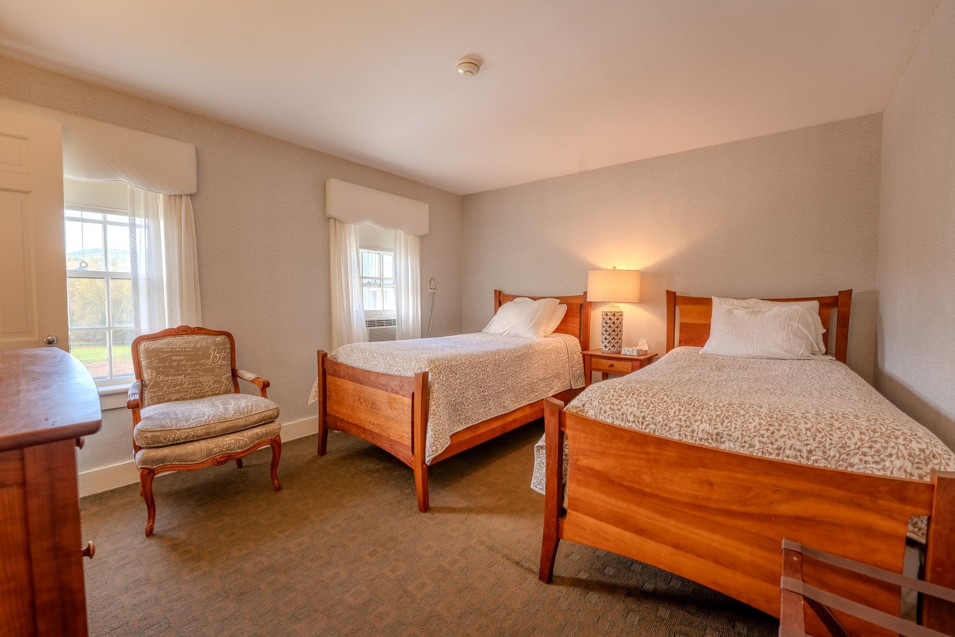 Bedroom with two twin beds, a floral armchair, and a wooden dresser.