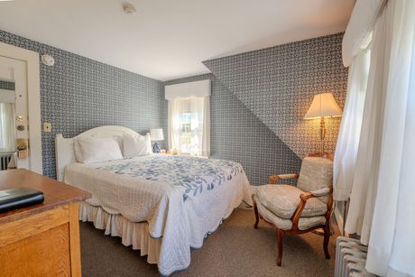 Bedroom with a bed, patterned wallpaper, armchair, and a window with white curtains.