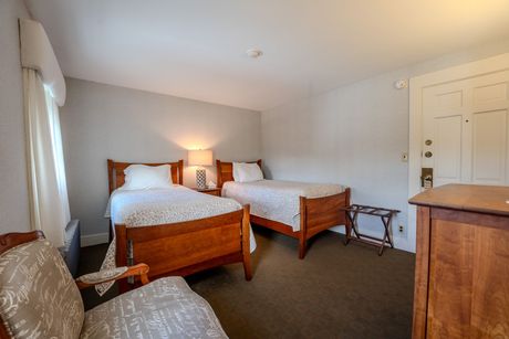 Bedroom with two twin beds, wood furniture, and a patterned chair. Neutral walls and carpet.