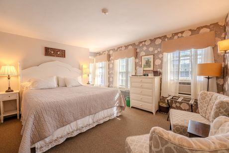 Bedroom with king bed, armchair, floral wallpaper, and windows.
