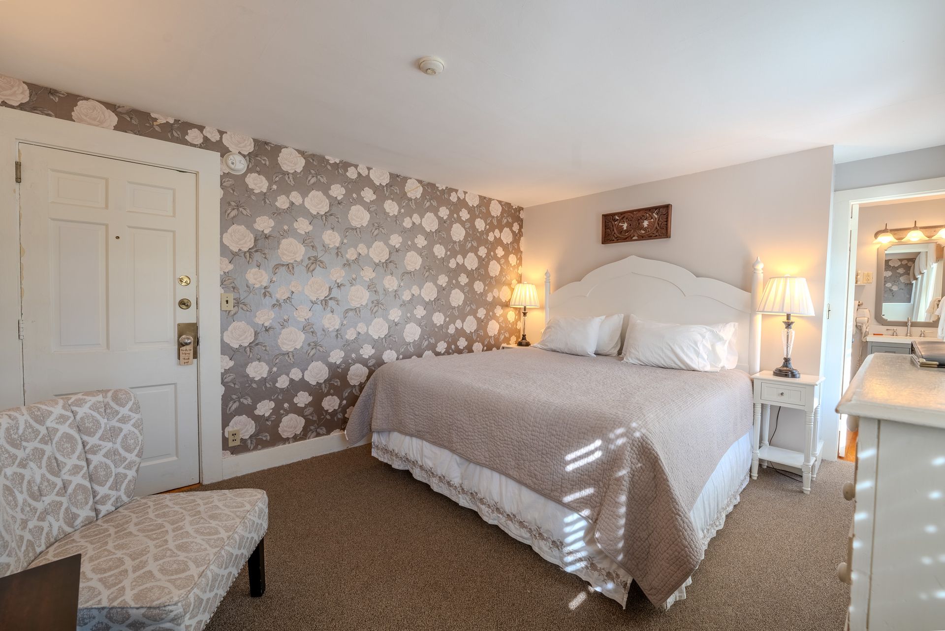 Bedroom with bed, patterned wallpaper, chair, and a bathroom entrance.