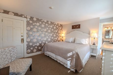 Bedroom with queen bed, floral wallpaper, small chair, and doorway to bathroom.