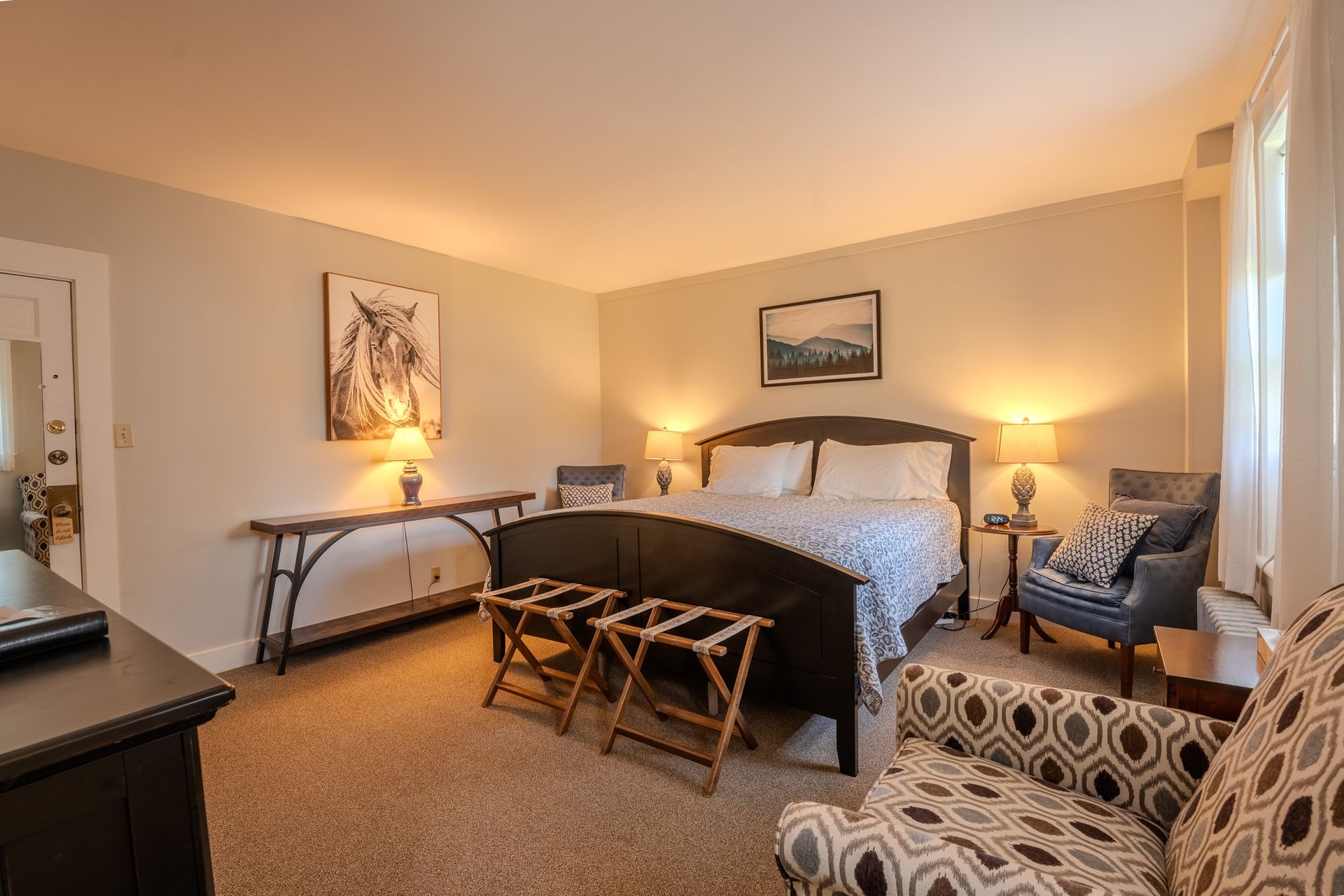 Bedroom with bed, chairs, luggage racks, lamps, and artwork.