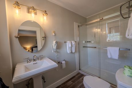 Bathroom with pedestal sink, shower, toilet. Gray walls, bright lights.