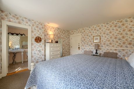 Bedroom with floral wallpaper, white dresser, and blue-patterned bedspread. A doorway leads to a bathroom.