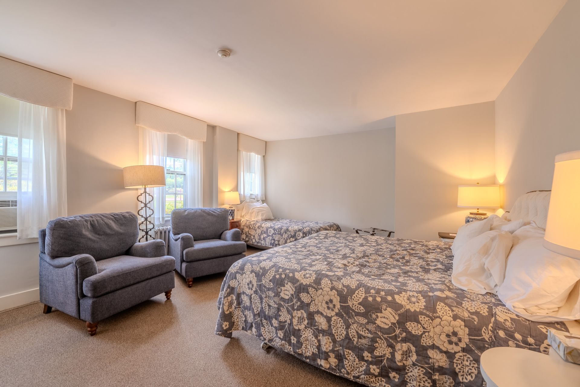 Bedroom with two double beds, two armchairs, and two lamps. Neutral colors.