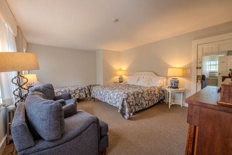 Bedroom with bed, loveseat, and two chairs, with lamps and doorway to another room, neutral color scheme.