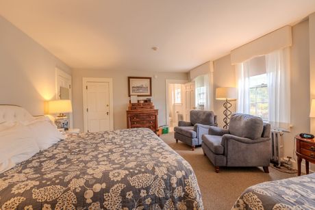 Bedroom with two beds, two armchairs, a chest of drawers, and a window.