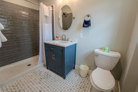 Bathroom with blue vanity, oval mirror, gray tiled shower, and white toilet.