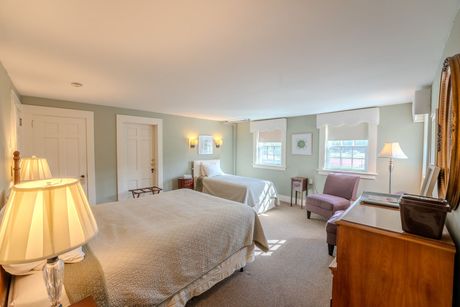 Bedroom with two beds, light green walls, wooden furniture, and windows.