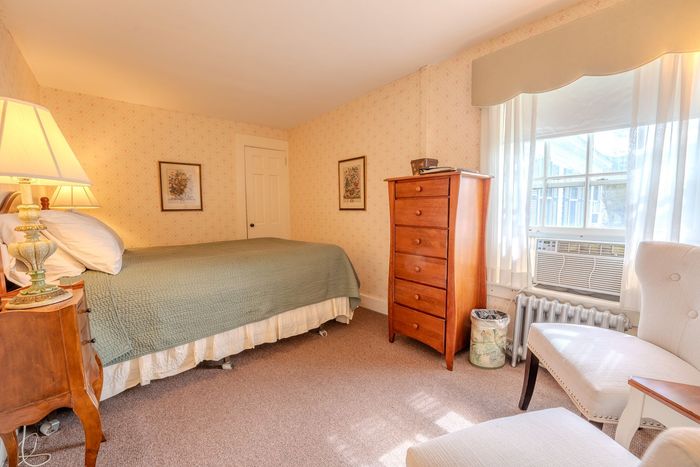 Cozy bedroom with a bed, dresser, armchair, window seat, and warm beige decor
