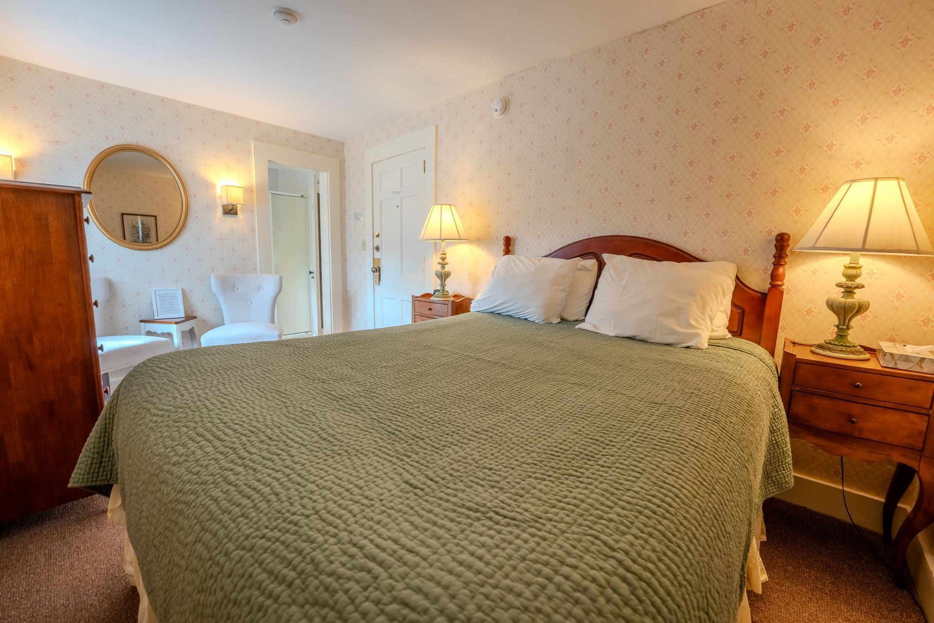 Bedroom with a bed, nightstands with lamps, a mirror, and a wardrobe; cream walls, wood furniture.