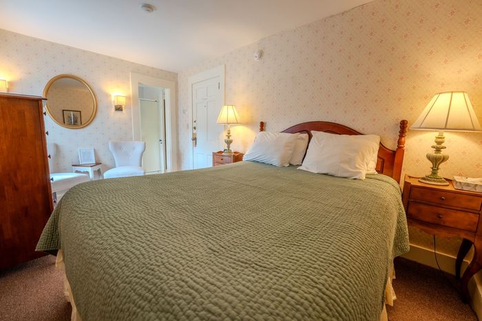 Cozy bedroom with green quilted bedspread, bedside lamps, and a vanity near an arched doorway