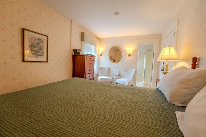 Bedroom with green bedspread, white pillows, dresser, chair, and warm lamp-lit decor