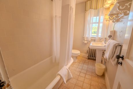 Bathroom with white tub, toilet, pedestal sink, and patterned tile floor.