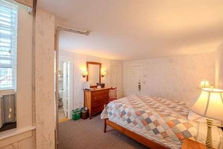 Bedroom with a bed, dresser, mirror, and a bathroom visible; warm lighting and patterned wallpaper.
