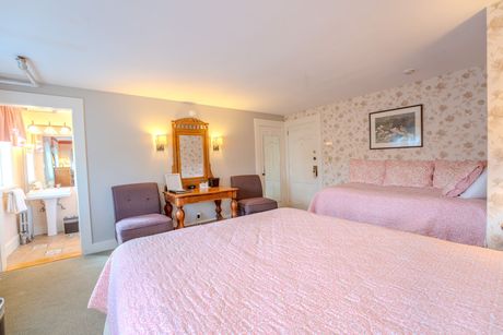 Bedroom with pink bedding, two chairs, vanity, and a daybed.