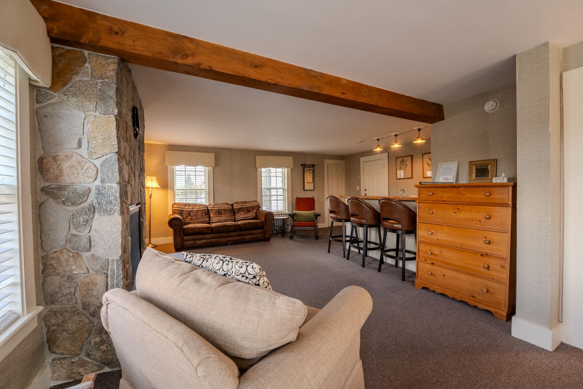 Living room with stone wall, wooden beam, brown sofa, and bar with stools.