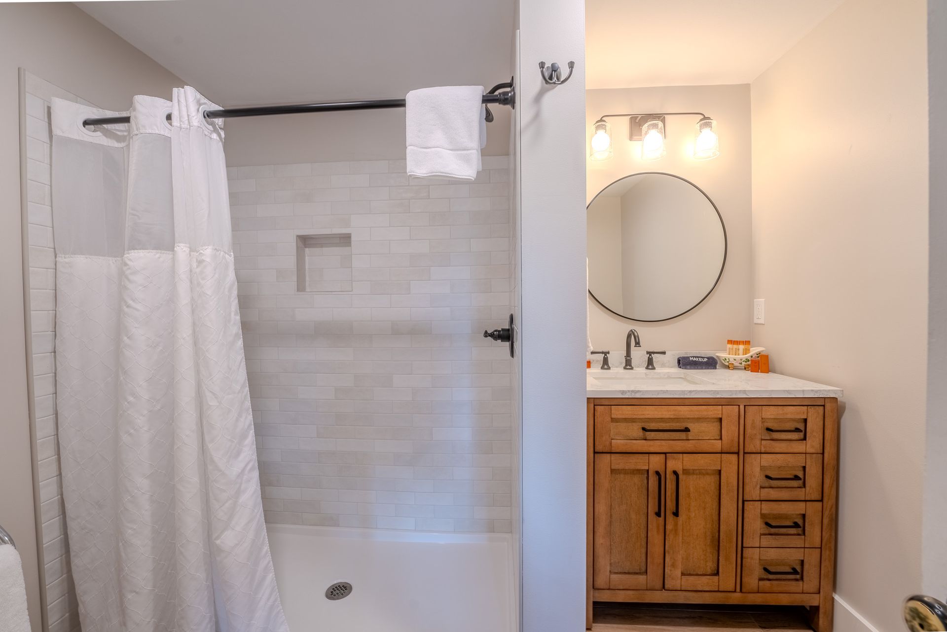 Bathroom with a shower and wooden vanity with round mirror.