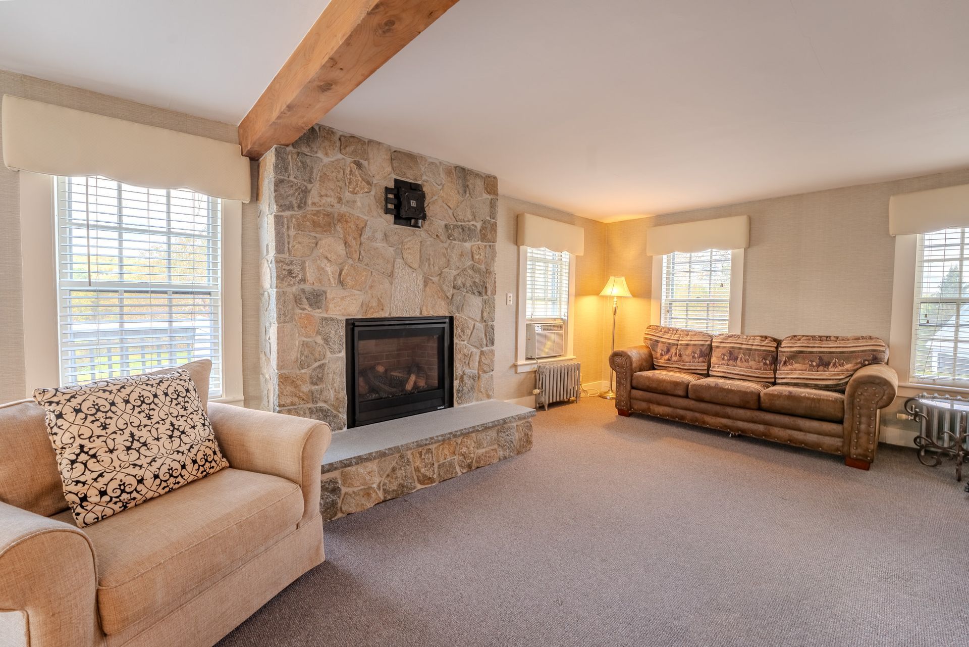 Living room with stone fireplace, beige walls, and a brown couch and chair.