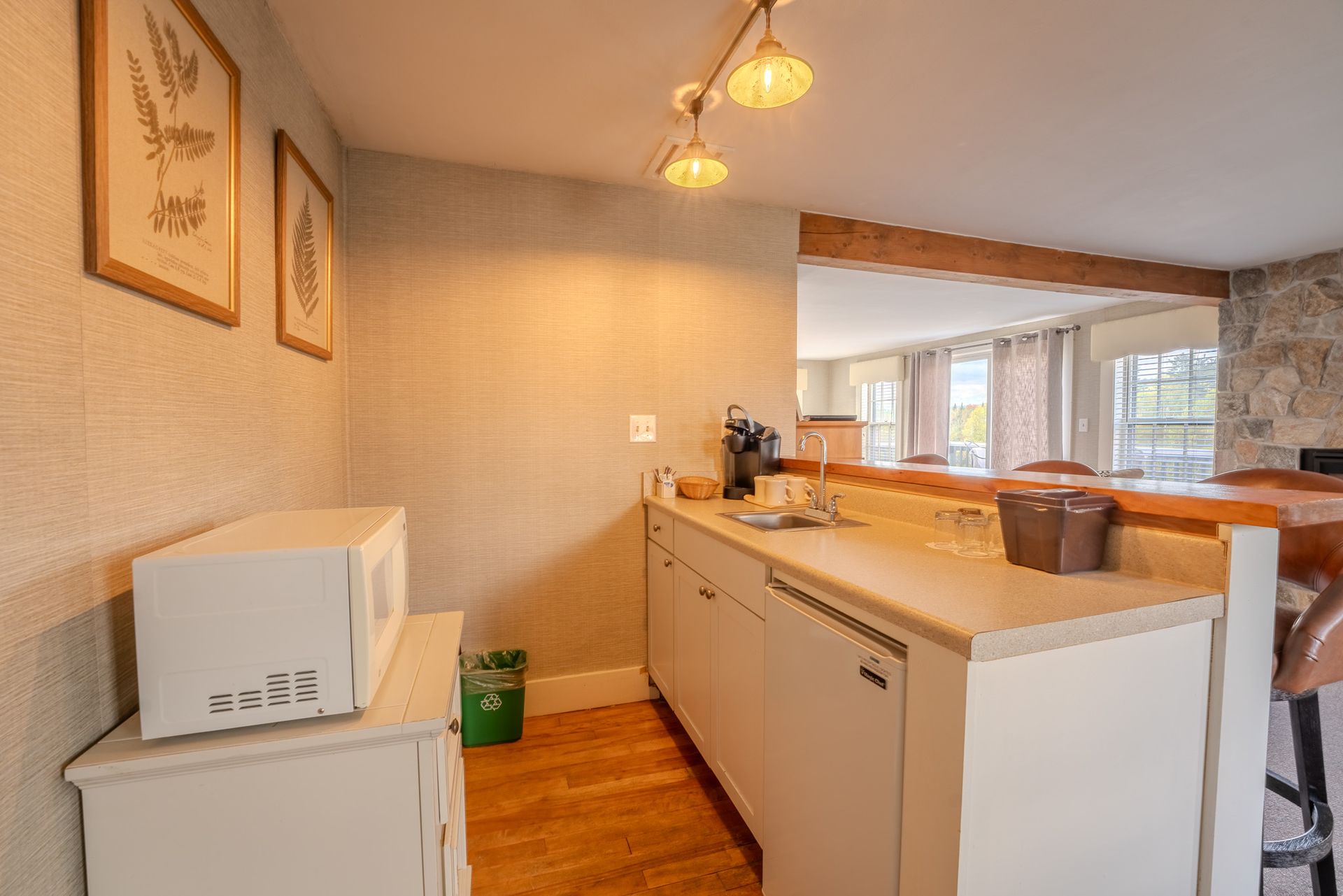 Small kitchenette with a microwave, sink, and cabinets, with a bar in the background.