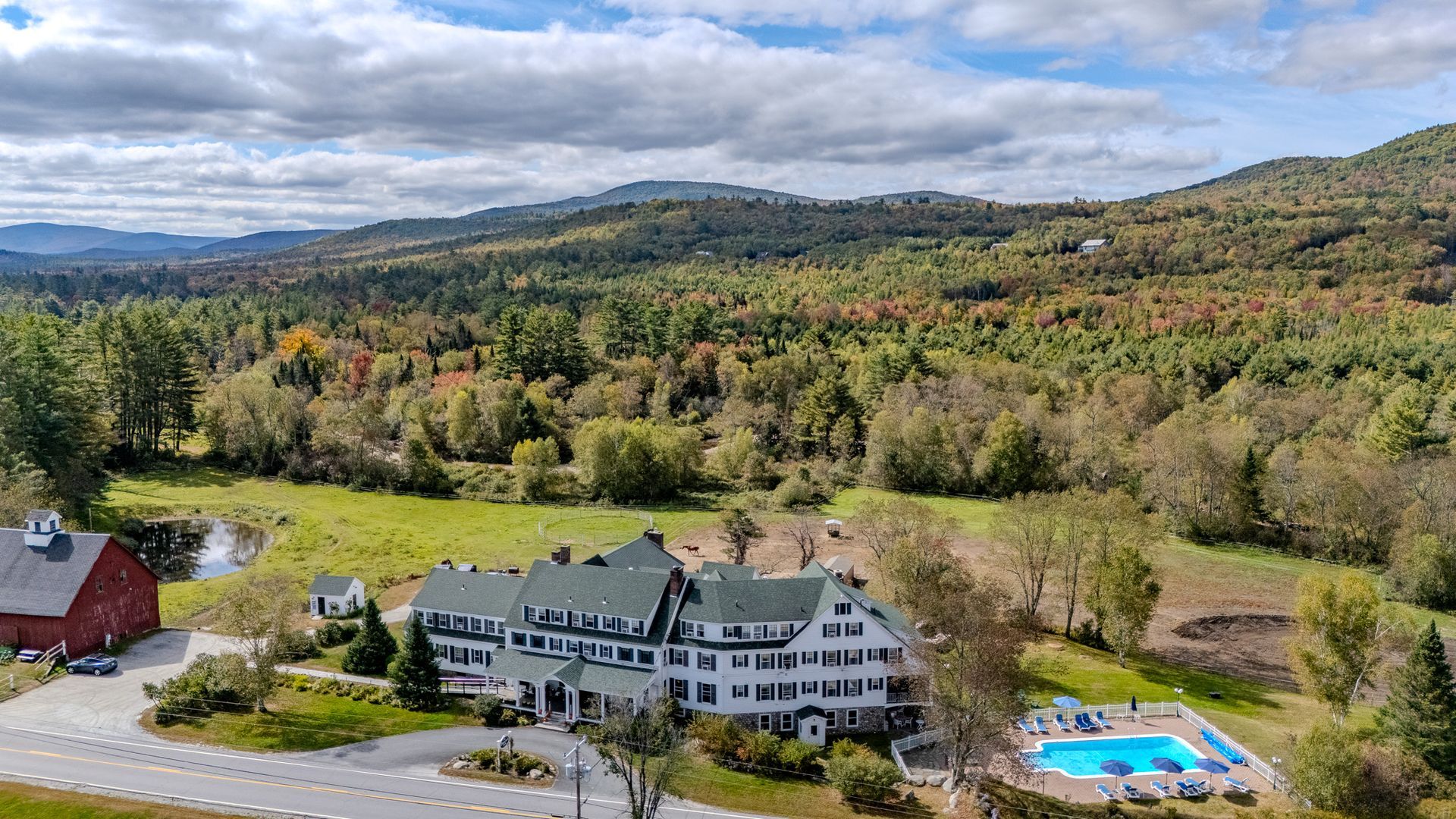 Hotel with pool nestled amidst fall foliage and mountain views.