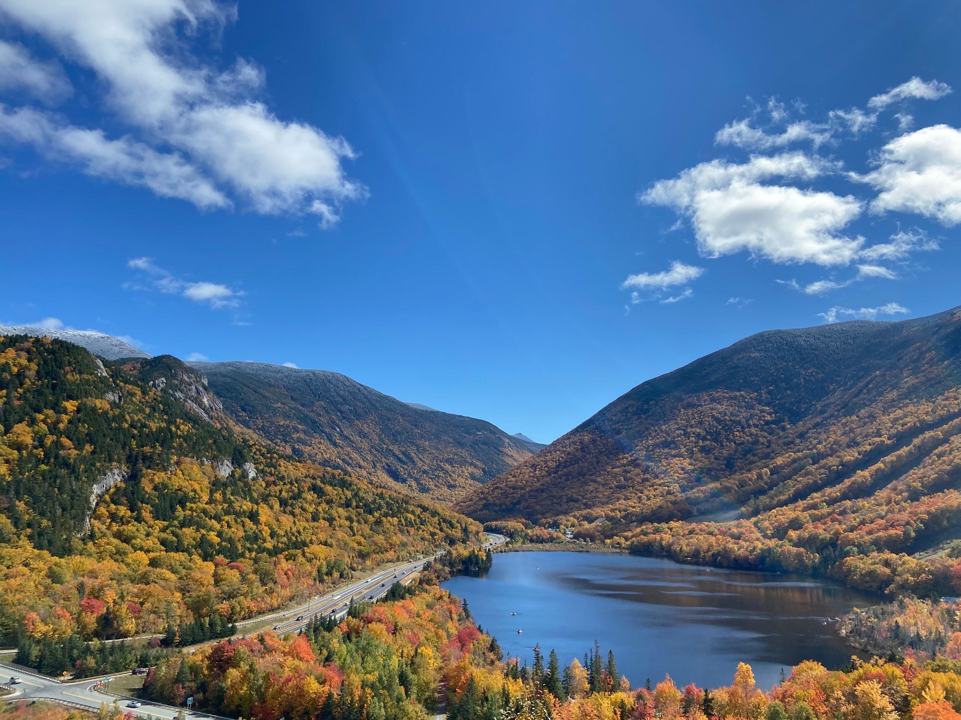 Autumn foliage surrounds a lake nestled between mountains under a bright blue sky.