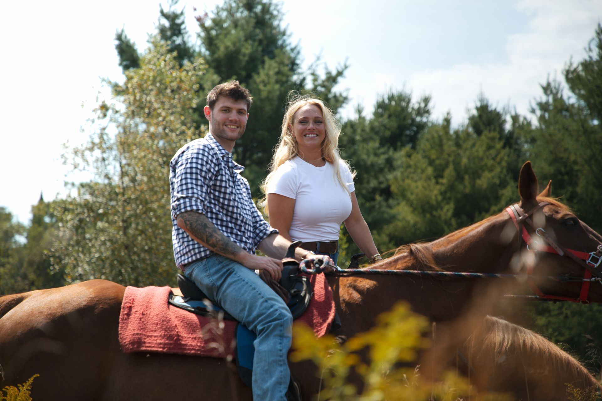 Two people riding a horse outdoors, with trees in the background.
